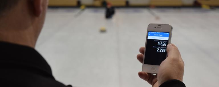 Person looking at rock hawk timer on iphone while rock is moving down the ice
